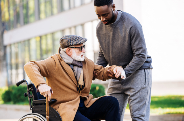 young man helping elderly man up out of wheelchair